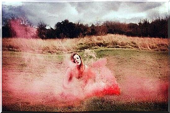 Woman sitting on grass with colored smoke.